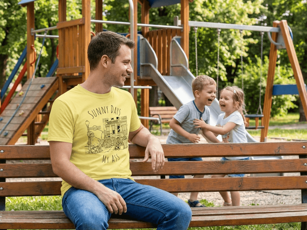 Man sitting on a bench with two children in a playground wearing sunny days t-shirt